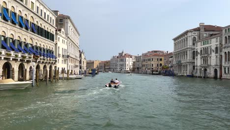 two rich italian men in private boat sailing between waterfront houses in grand canal, venice, italy