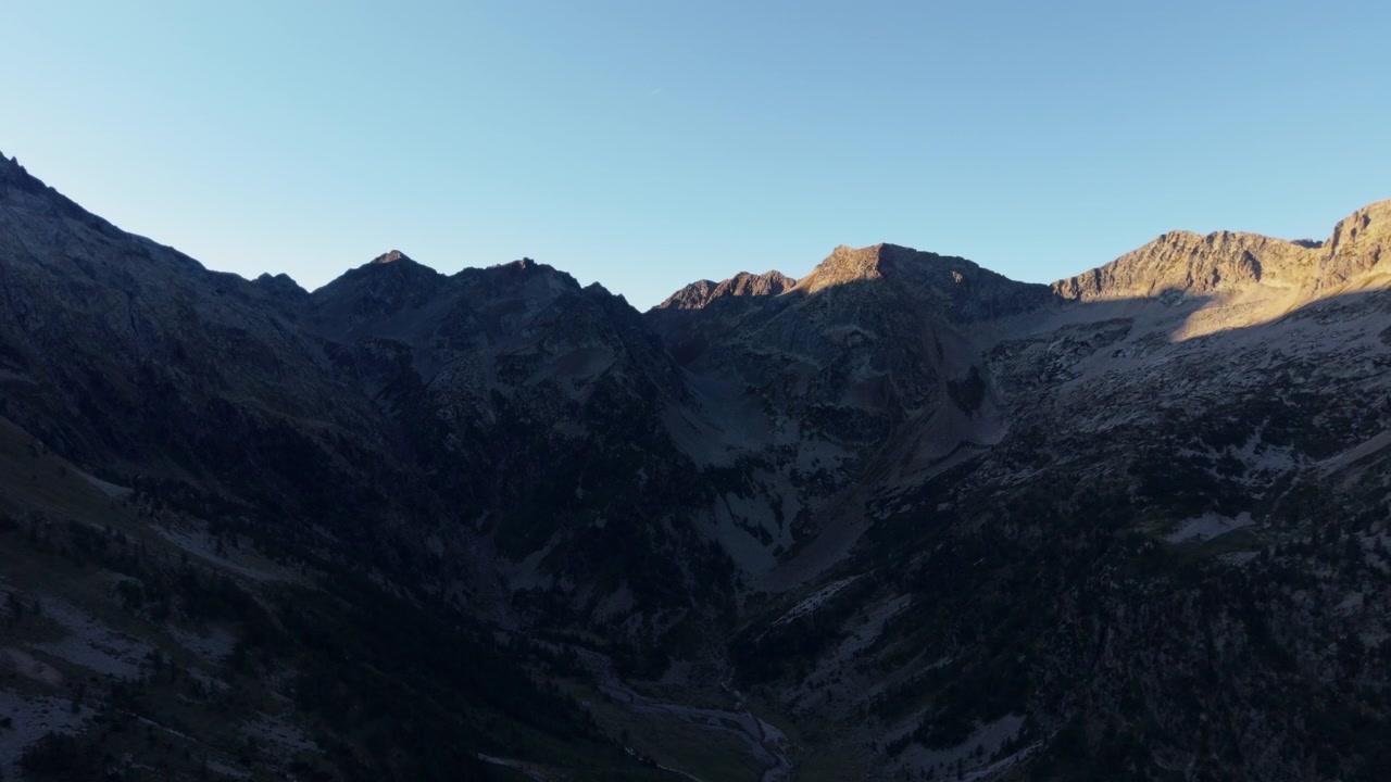 Sunlight illuminates rugged Dolomites peaks under clear sky at sunset, aerial view