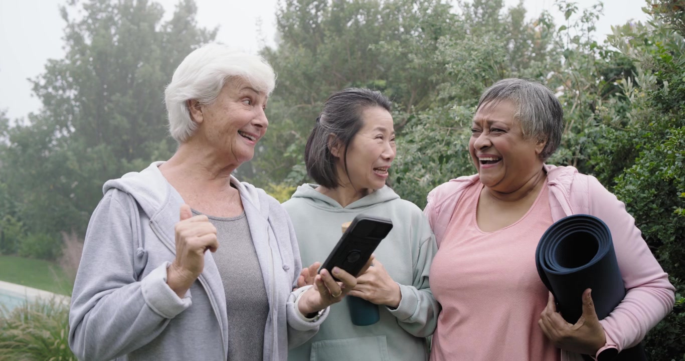 Diverse amiche che guardano una donna anziana mostrare lo smartphone, condividendo un messaggio divertente e ridendo