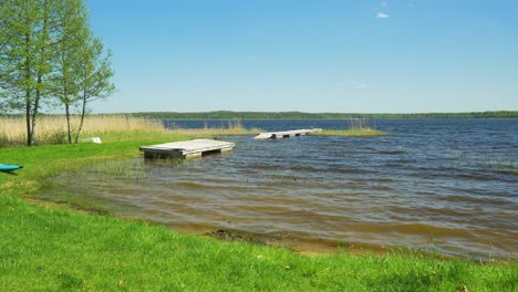 Beautiful-view-of-a-Lake-Usma-shore-on-a-sunny-summer-day,-distant-islands-with-lush-green-forest,-rural-landscape,-coast-with-old-distant-reeds,-wood-pier,-wide-shot