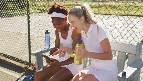 Video of happy diverse female tennis players sitting, talking and resting after match