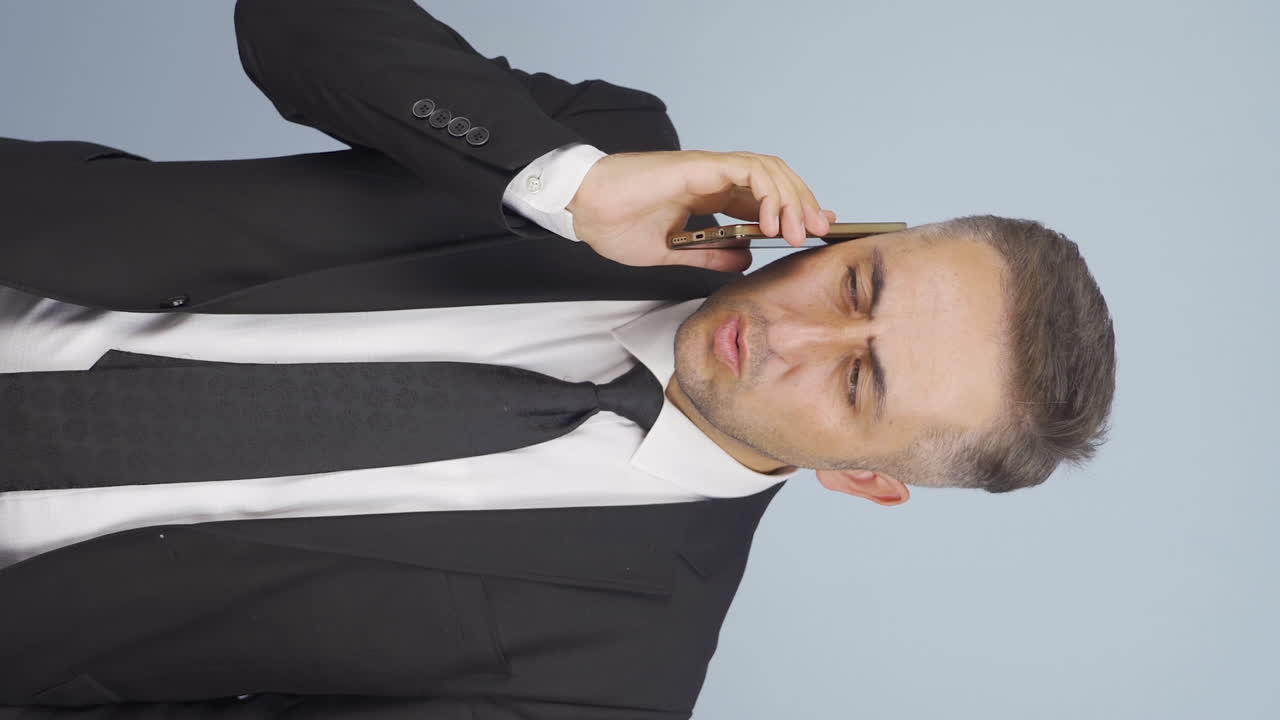 video vertical de un hombre de negocios siendo interrumpido y enojado mientras habla por teléfono.