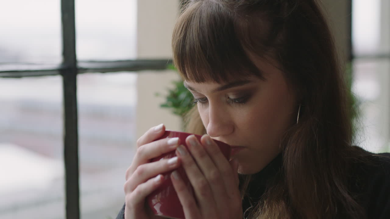 retrato elegante joven mujer caucásica estudiante bebiendo café en casa mirando por la ventana pensando en el futuro disfrutando de un estilo de vida relajado