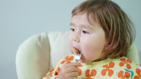 little girl eating tasty golden crispy chicken breast nuggets sitting in baby chair at home