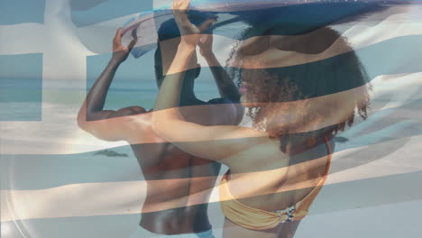 animación de la bandera de grecia sobre una pareja afroamericana con una tabla de surf en la playa