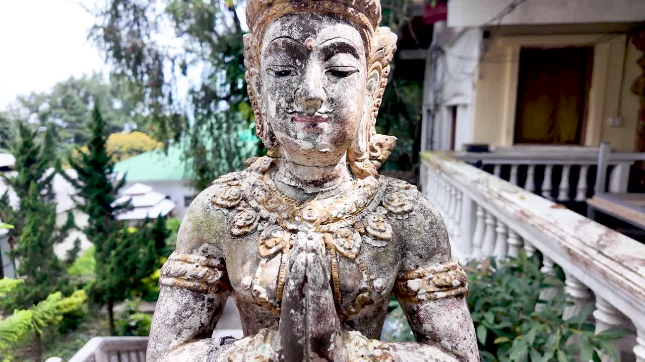 Weathered statue of Buddha in prayer position bringing a sense of ancient spirituality and peace to a garden setting