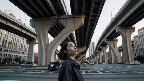 young woman stands with closed eyes under a highway overpass, taking a moment of contemplation amidst the urban environment, surrounded by cars and buildings