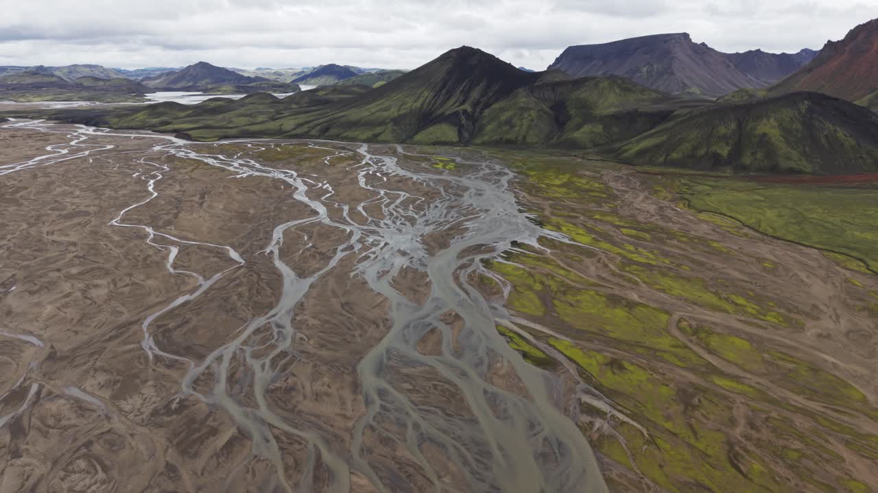 Volo aereo con drone sopra i tortuosi fiumi glaciali e le vivaci montagne di riolite di Landmannalaugar, Islanda