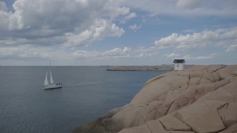 small house on the coast in sweden on a rock with sailboat driving by