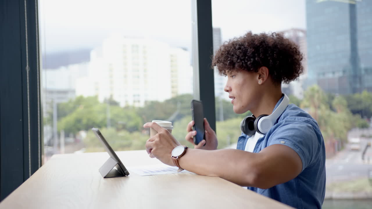 Talking on smartphone, man with headphones using tablet and drinking coffee