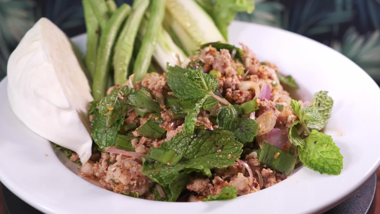 auténtico moo larb tailandés con menta y especias recién cocinadas girando sobre un plato blanco de cerca