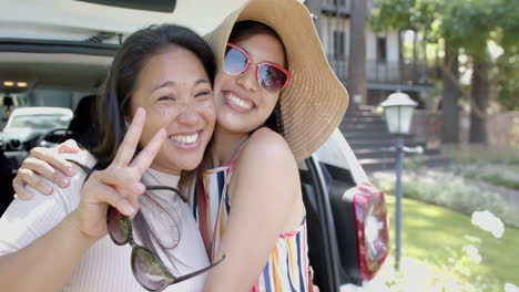 happy asian female friends with sunglasses and sun hat sitting in car trunk and smiling, slow motion