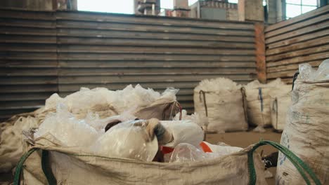 a brunette man in a white protective uniform in a safety helmet and an orange vest jumps into a large pile of recycled plastic cellophane at a waste processing and sorting plant