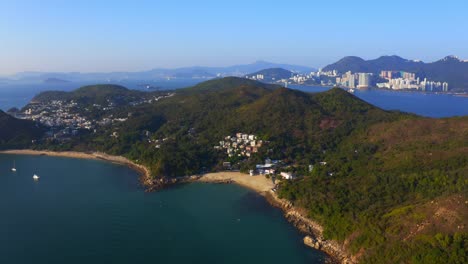 disparo de un dron que viaja hacia adelante sobre una isla tropical con algunos pueblos y una playa entre las montañas y el bosque durante un día soleado-2