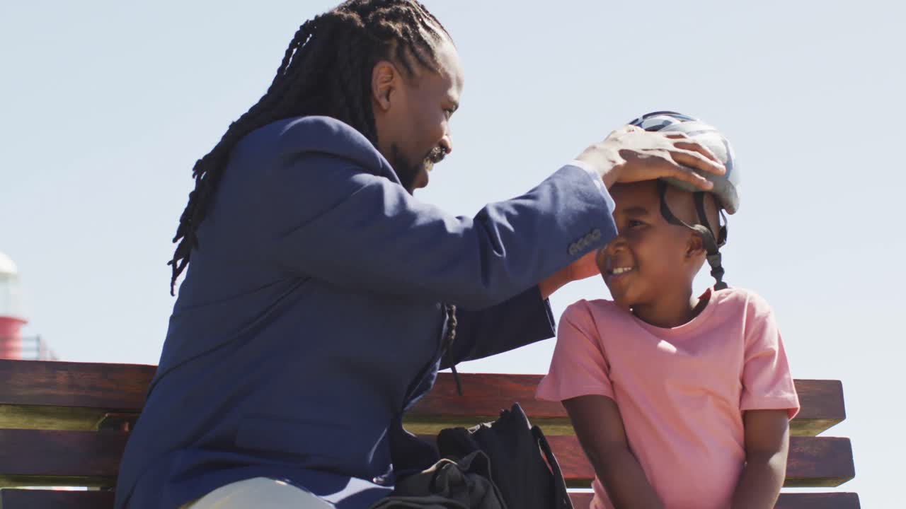 video de un feliz padre afroamericano poniendo casco en la cabeza de su hijo