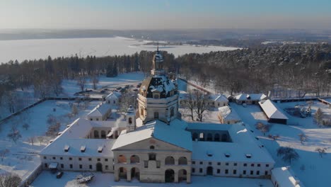 Aerial-view-of-the-Pazaislis-monastery-and-the-Church-of-the-Visitation-in-Kaunas,-Lithuania-in-winter,-snowy-landscape,-Italian-Baroque-architecture,-flying-around-the-tower,-lake-in-the-background