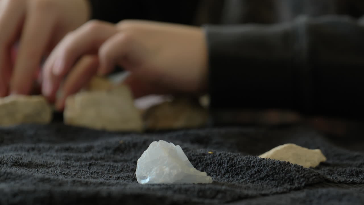 한 어린 소년이 탁자 위에 있는 자신의 암석 컬렉션을 보고 나머지는 배경에 있는 빨간색 석영 암석을 움직입니다.