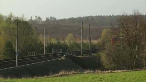 Red-Deutsche-Bahn-freight-train-moving-along-tracks-in-rural-area,-late-afternoon-light