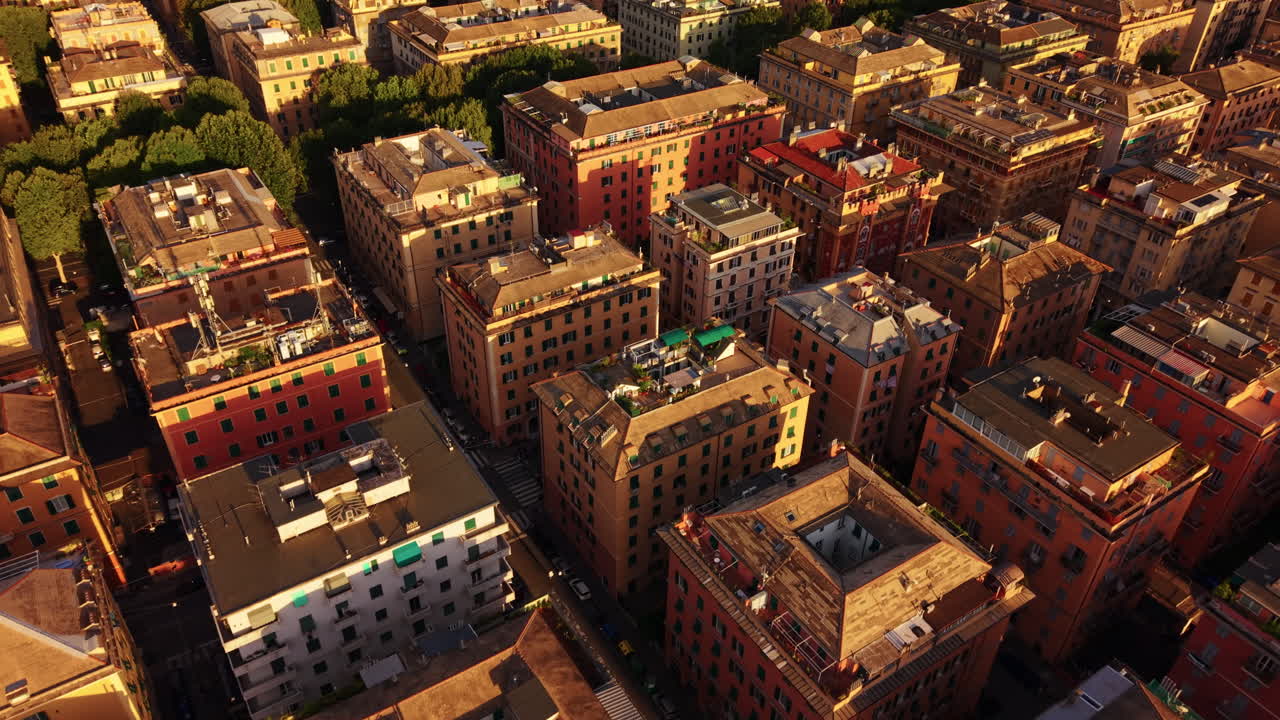 Drone descends in forward motion above Genoa’s colorful buildings and trees at sunset