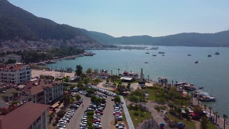 aerial dolly of city with many cars parked, boats docked at the coast, buildings, mountains in the back and small park with an obelisk