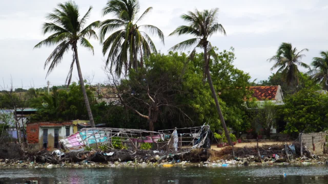 Tilt-up reveal shot of dilapidated house and garbage area on river bank of Son Hai