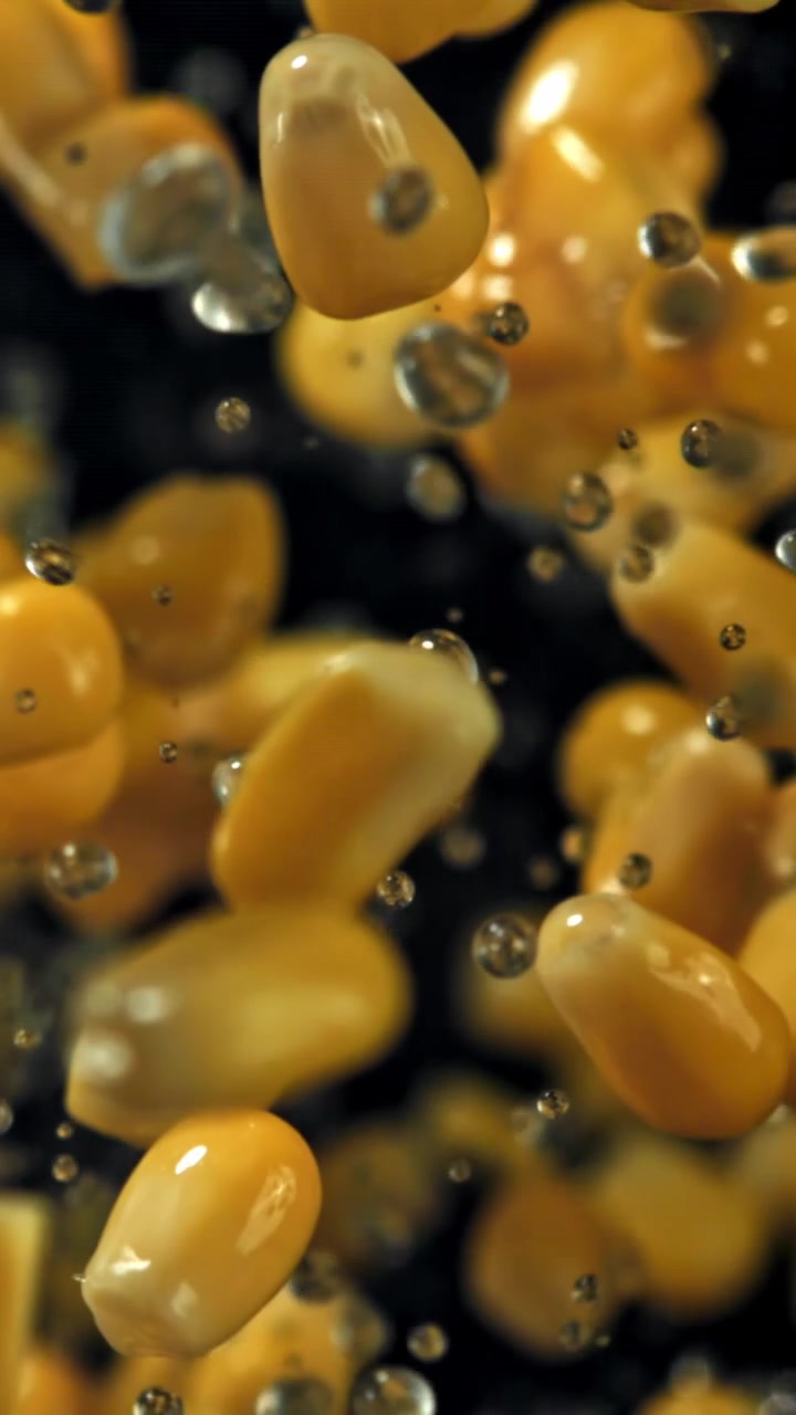 Chicchi di mais gialli che galleggiano nell'acqua con bolle al rallentatore