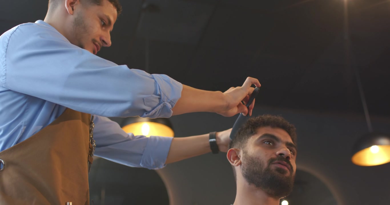 Mandlig barber trimmer mandlig kundes hår med trimmer og kam i barbersalon efter kundens ønske