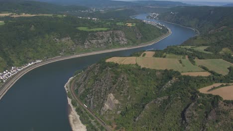 winding blue river with a green barge set against a lush green valley, fields, and distant town, bordered by a road and cliff