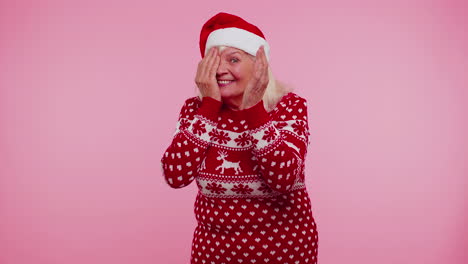 Woman-in-sweater-Santa-Christmas-hat-fooling-around-having-closing-eyes-with-hand-and-spying-through