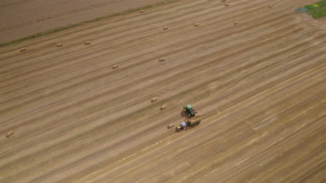 Farmer-making-cargo-with-hay-bale-pile-in-tractor-trailer,-drone-view
