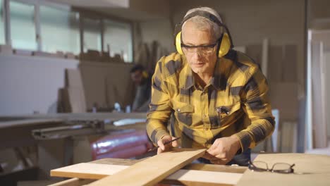 adult carpenter man working in carpentry workshop measures wood with meter.