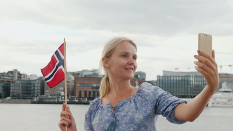 a young woman with a norwegian flag photographes herself against the background of the oslo city lin