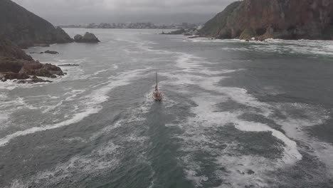 el barco cruza la espumosa barra del río knysna en condiciones de cielo nublado plateado.