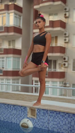 woman practicing yoga by the pool on a rooftop terrace