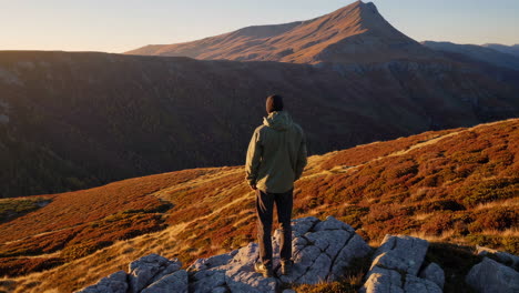 hiker standing on a mountain peak admiring a vast autumn landscape at sunset