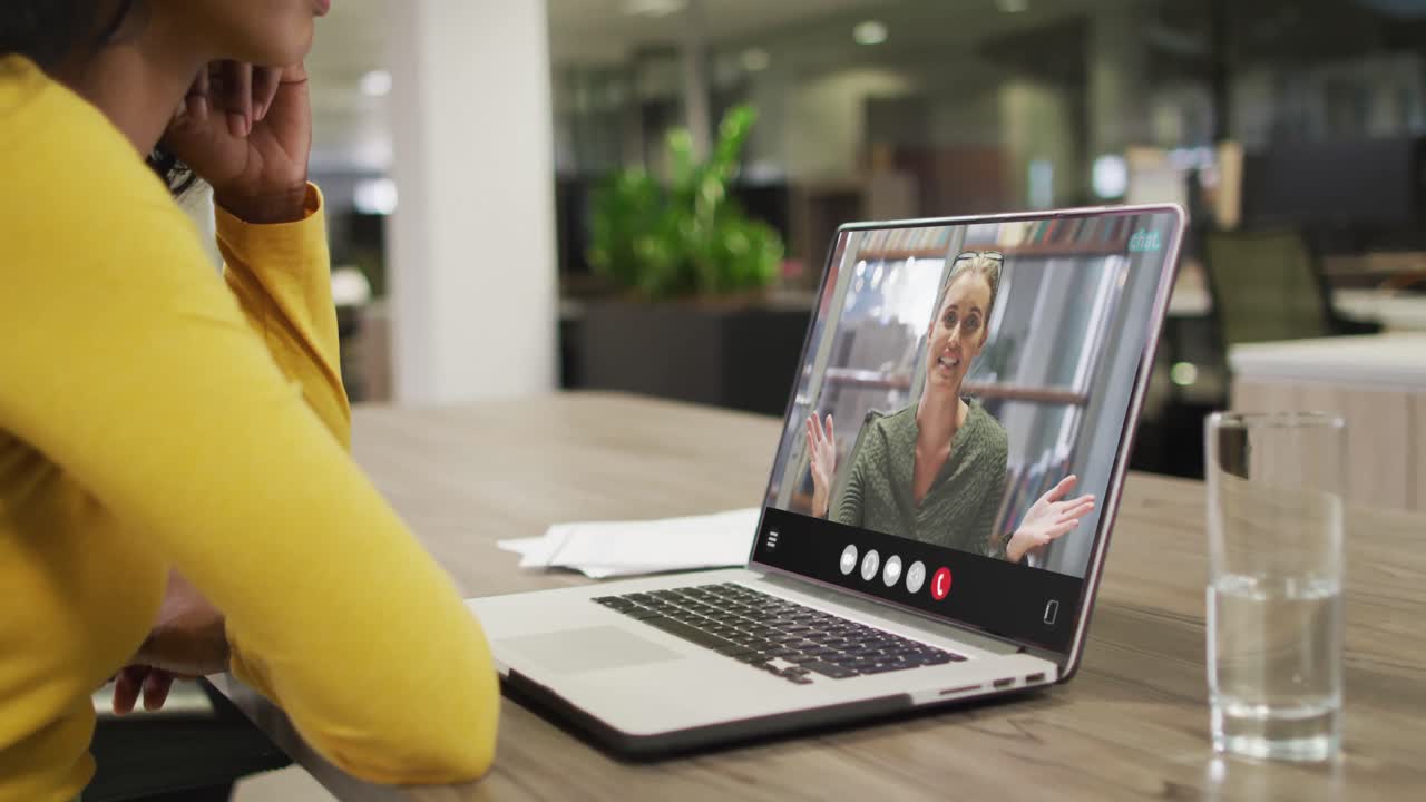Biracial woman using laptop for video call, with business colleague on screen