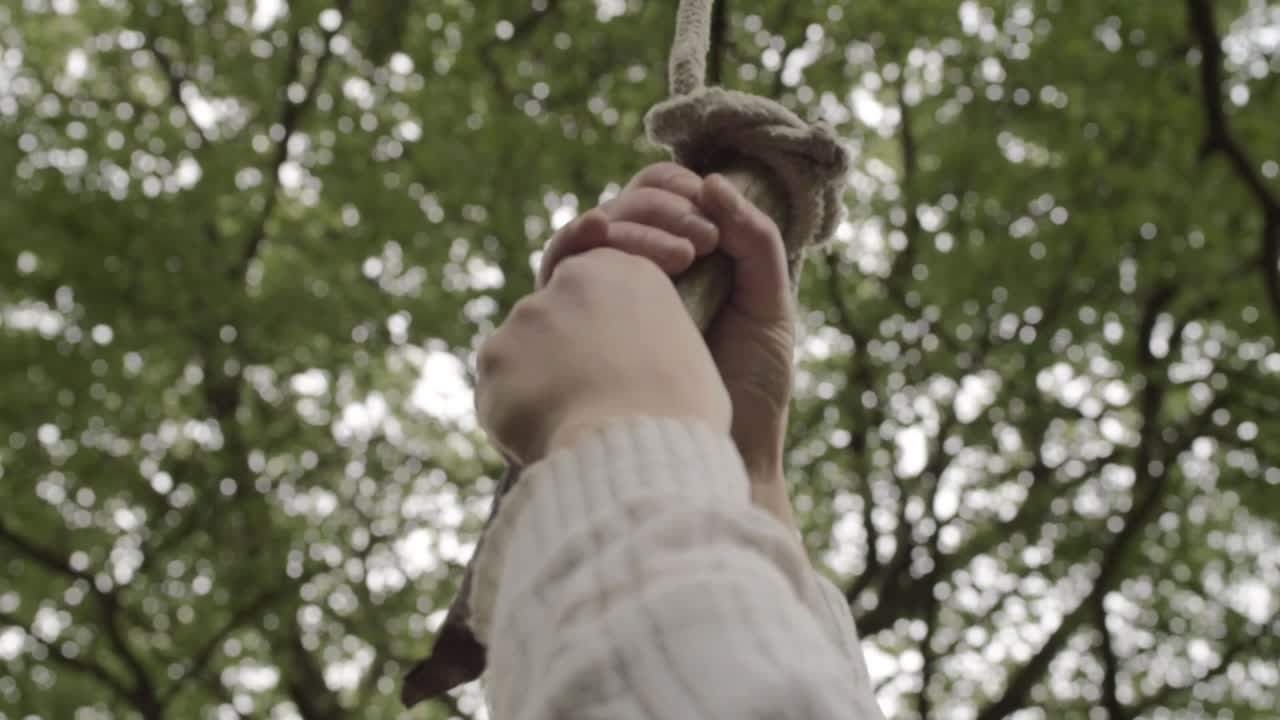 Hands holding a homemade rope swing in countryside