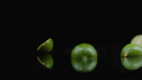 Zwei-Reife,-Geschnittene-Grüne-Limetten-Fallen-Auf-Glas-Mit-Wasserspritzern-In-Zeitlupe-Auf-Dunklem-Hintergrund