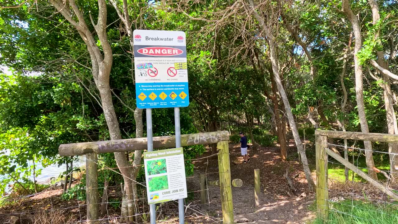 Daylight camera pan past warning signs, trash bins, and greenery in a Phuket riverside park