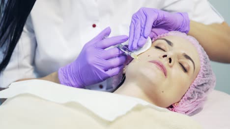 beautician makes a skin prick on face for young woman using syringe with needle in salon. facial injection procedure