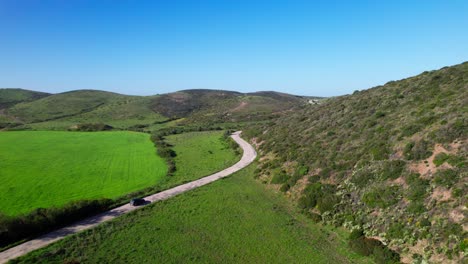 car driving on unpaved road along the grassy fields in mountainous area. - aerial shot