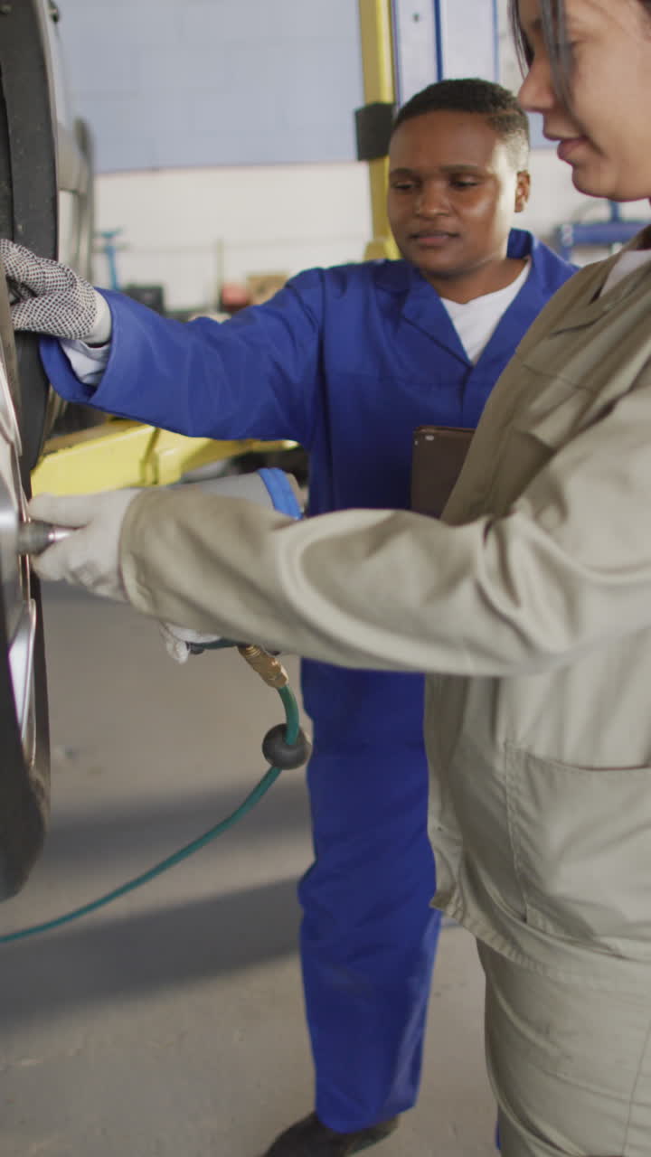 video vertical de dos mecánicas de automóviles diversas cambiando el neumático