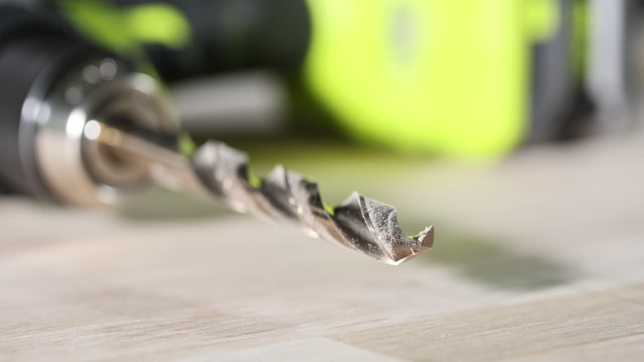 Close-up of a drill bit with a power drill in the background