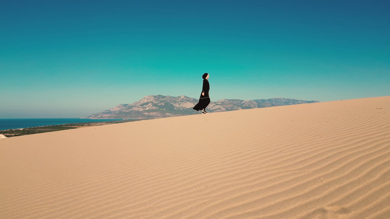 mujer en abaya negra en una duna de arena