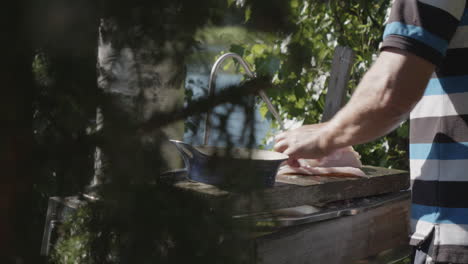 static view form one side of man filleting fish in the woods in front of lake