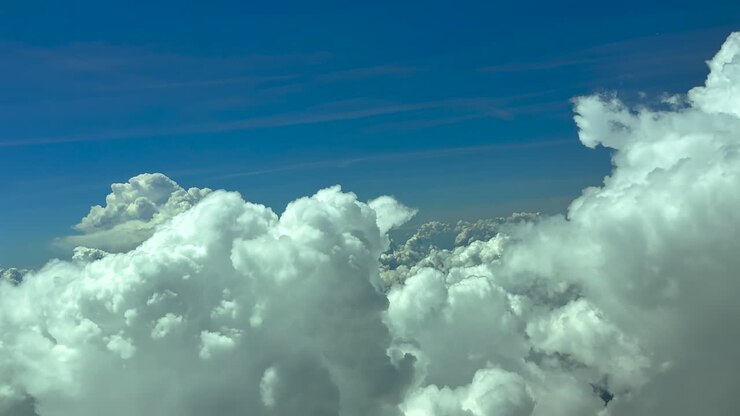 Immersive pilot’s eye view from inside a jet cockpit while flying peacefully between the tops of storm cumulonimbus clouds in a blue sky.. Scene teken at 12000m high