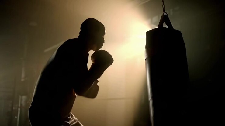 Silhouette di un pugile che si allena con un sacco da boxe in una palestra buia