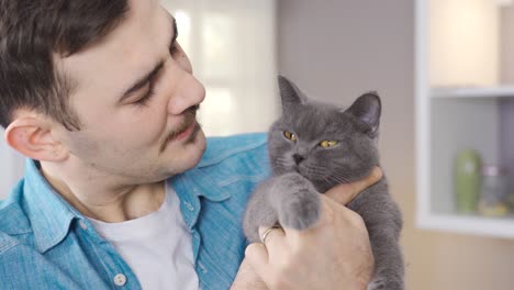 the man holds his gray cat in his lap and looks at him affectionately.