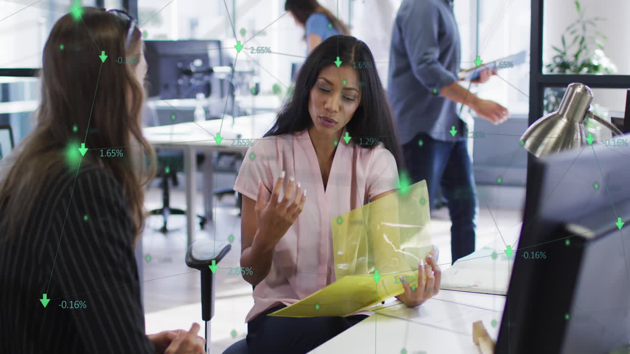 Network of connections floating against two diverse female office colleagues discussing at office