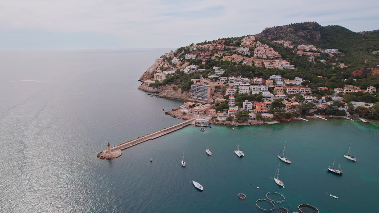 Epic wide aerial circling the iconic Port d'Andratx lighthouse and coastal homes on the island of Mallorca, Spain, a popular Mediterranean vacation destination for sailing, fishing and dining